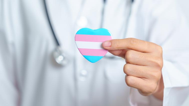 Health care provider with stethoscope holding heart shape with transgender flag colors